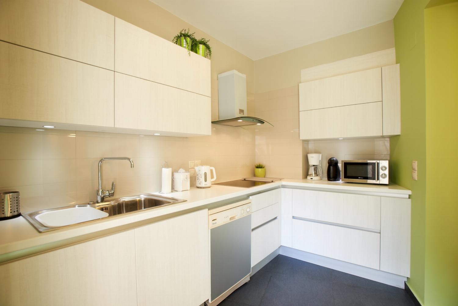 A modern kitchen features sleek white cabinetry, integrated stainless steel appliances, dark floor tiles, and a light green accent wall.